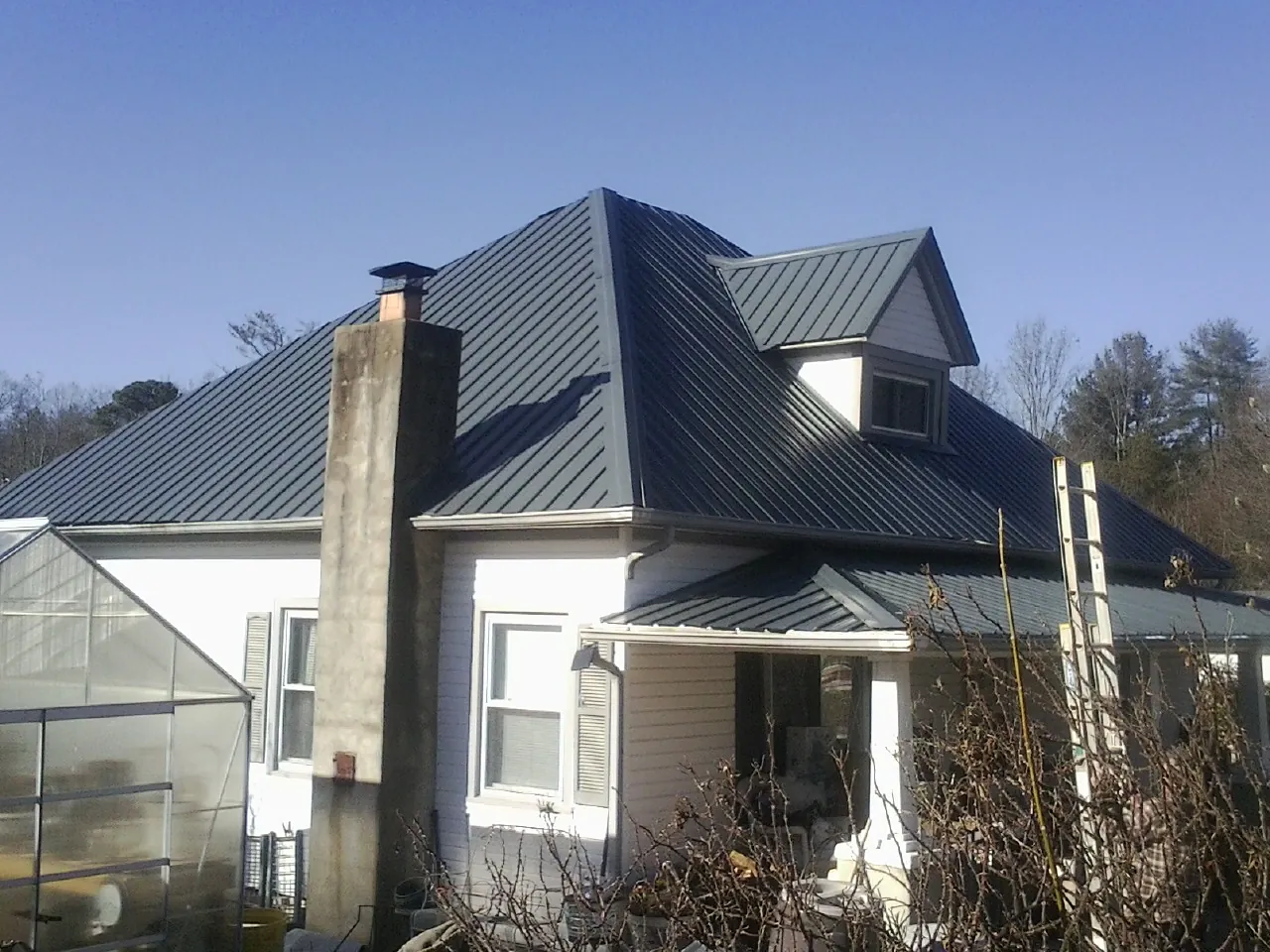 Dark blue standing seam metal roof on a white farmhouse with dormer — Slate & Tile Roof Repair by Roofing Brothers in Carrboro