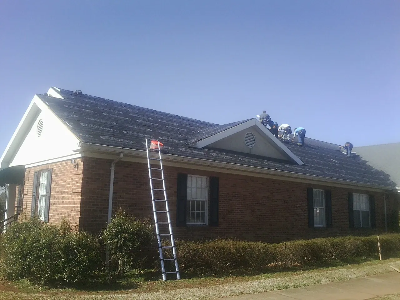 Crew tearing shingles off a brick ranch roof with a ladder set — Emergency Roof Repair work by our crew in Carrboro