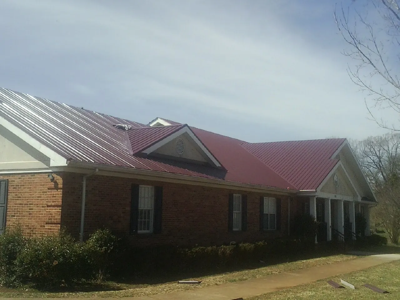 Red metal roof with gabled entries on a long brick building, from a Hail Damage Roof Repair job in Carrboro