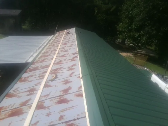 Old rusted panels beside newly installed green metal roofing — Wind Damage Roof Repair by Roofing Brothers in Carrboro