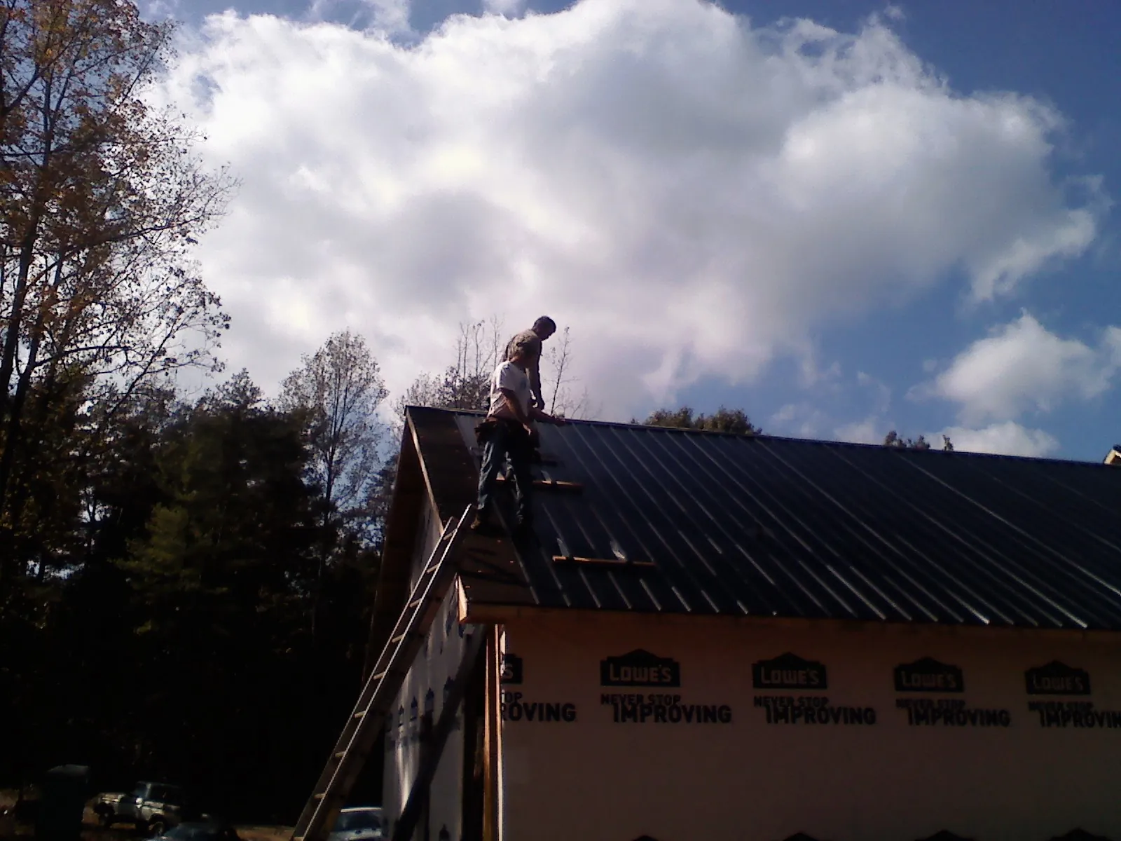 Roofer fastening dark metal panels high against a cloudy sky, from a Roof Inspection job in Carrboro