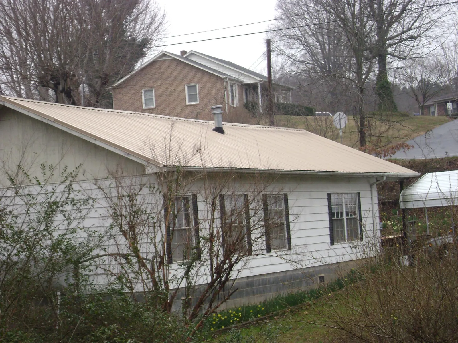 Tan metal roof on a white sided house set into a hillside — Commercial Roofing by Roofing Brothers in Carrboro
